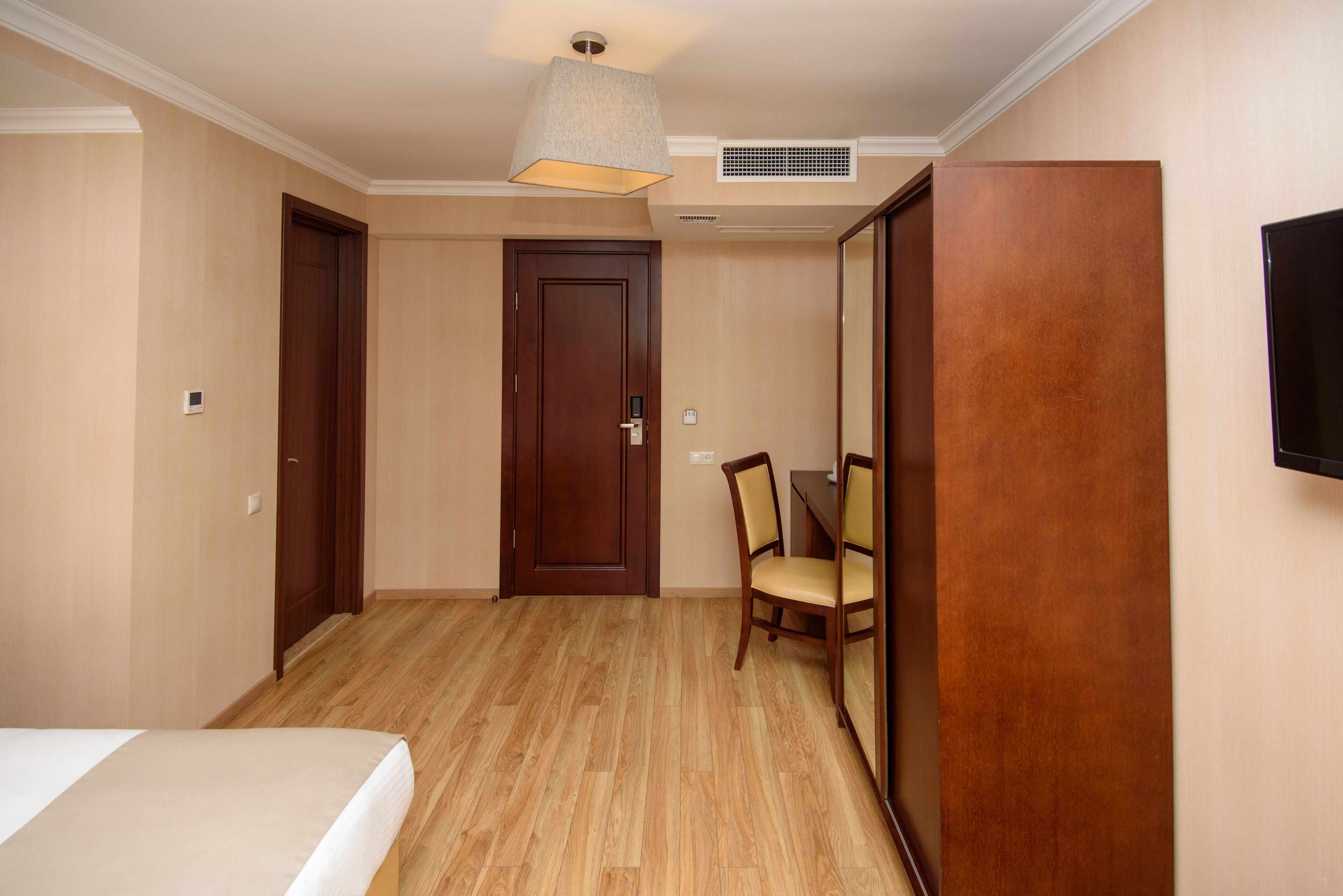 A hotel room with a bed, a wooden door, a chair, and a table.