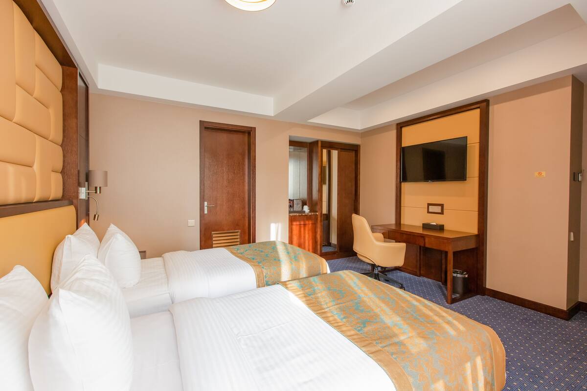 A hotel room with two beds, a desk, a chair, a television, and a bathroom door.