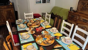Una mesa de comedor dispuesta con platos, tazas y pasteles, rodeada de sillas y un sofá verde.