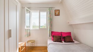 Un dormitorio con cama, una mesita redonda y una ventana con cortinas.