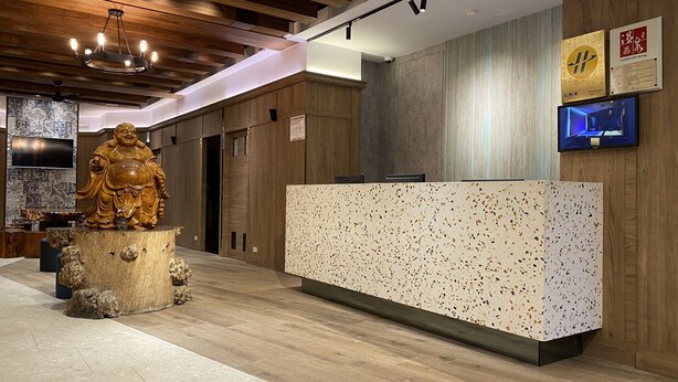 A reception area with a wooden reception desk, a large statue, and a television screen. - Jinspa Resort Hotel (New Taipei City)