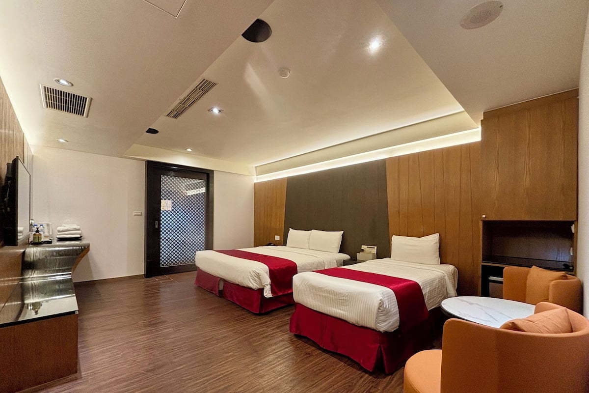 A hotel room with two beds, a desk, a chair, and a TV.