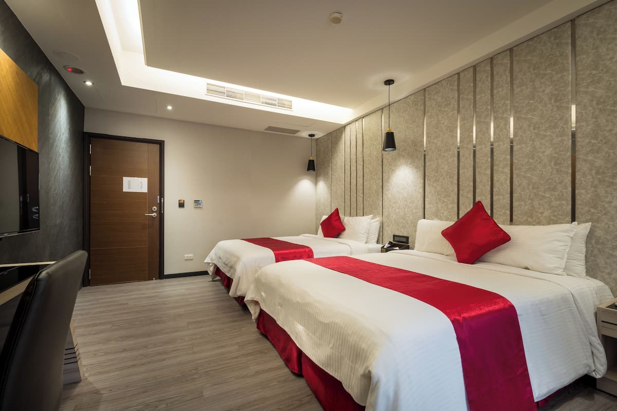 A hotel room with two beds, a desk, and a TV.
