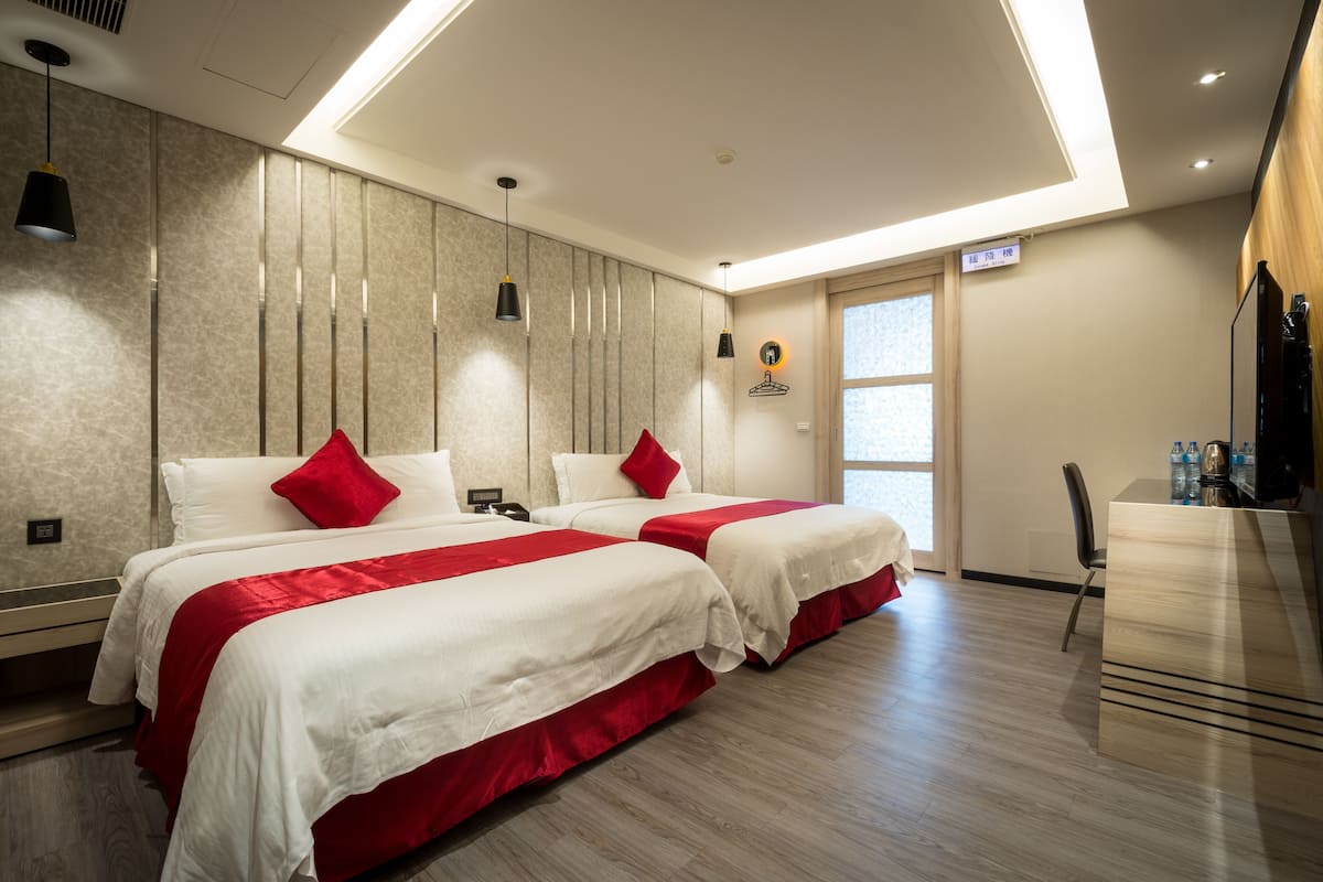 A hotel room with two beds, a desk, and a chair.