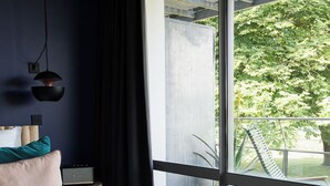 A modern bedroom with a large bed, a bedside table, a lamp, and a view of a balcony with outdoor furniture. - Auberge Basque (Saint-Pee-sur-Nivelle)