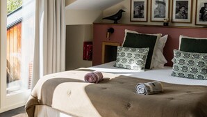 A bedroom with a large bed, a window with curtains, a wooden ceiling, and framed pictures on the wall. - Auberge Basque (Saint-Pee-sur-Nivelle)
