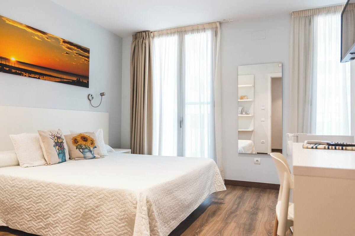 Habitación de hotel con una cama grande, un escritorio y una silla. Hay un cuadro en la pared y una ventana con cortinas.