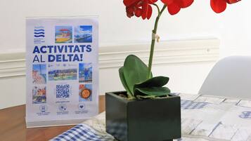 Una taula amb una orquídia vermella en test, un cartell amb activitats al Delta i un mantell de taula amb quadres.