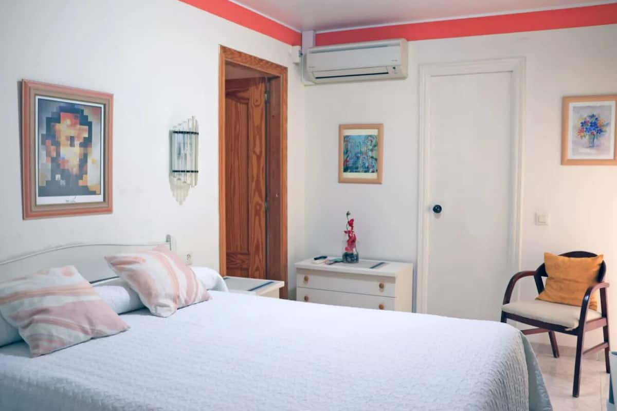 Un dormitorio con cama, mesita de noche, silla y puerta.