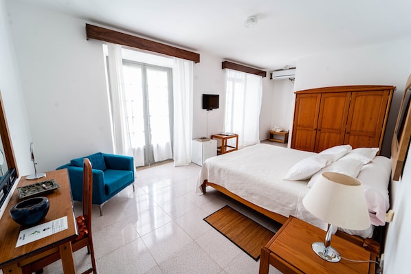 A hotel room with a bed, a desk with a chair, a TV, a wardrobe, and a window with curtains. - Boutique Hotel Praia Maria (Praia)