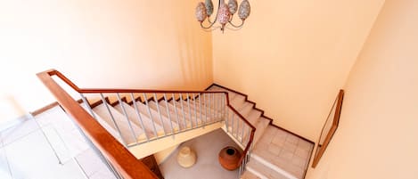A staircase with a wooden handrail, a chandelier, and a woven basket on the floor.