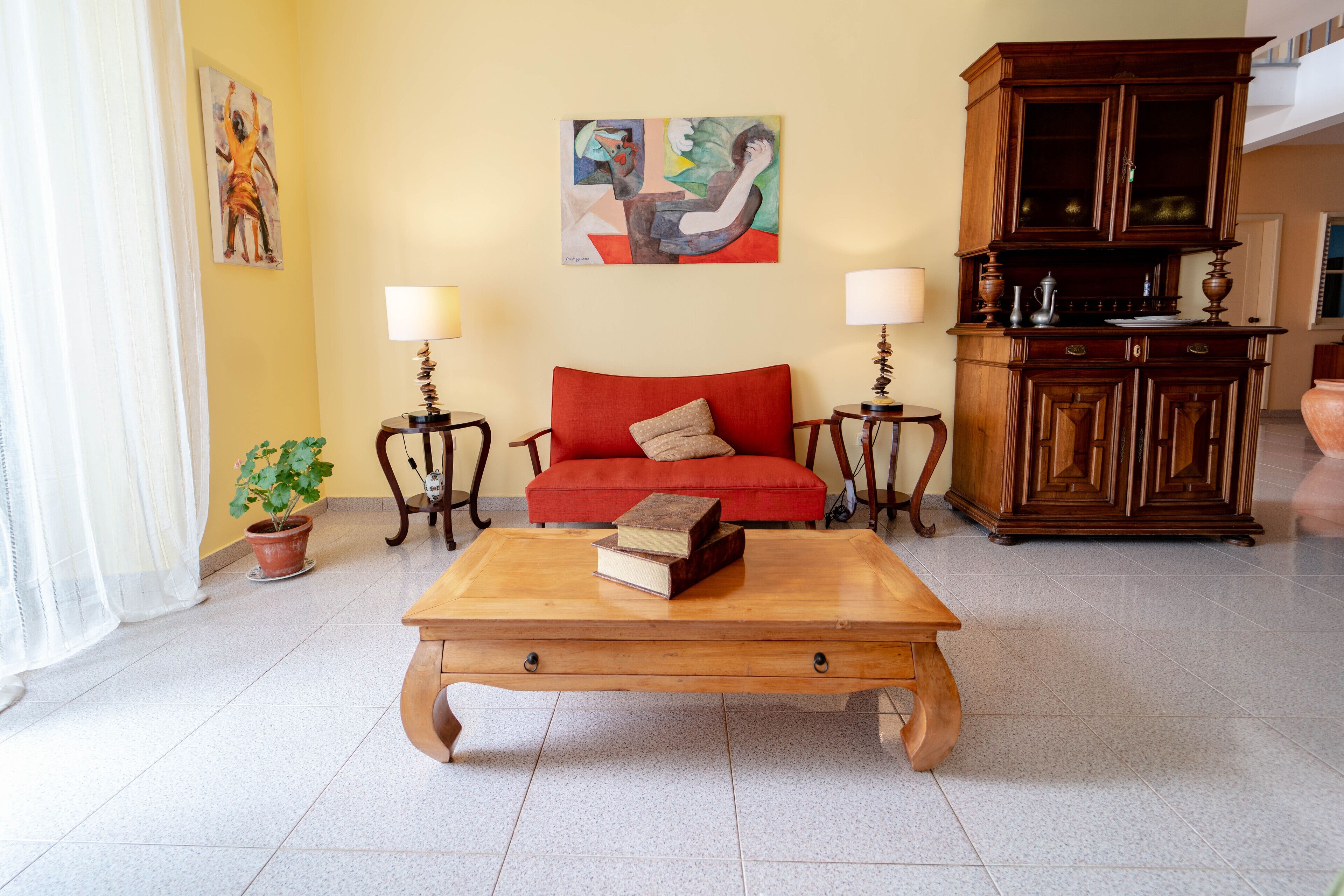 A living room with a red sofa, wooden coffee table, two side tables with lamps, a cabinet, and a painting on the wall.