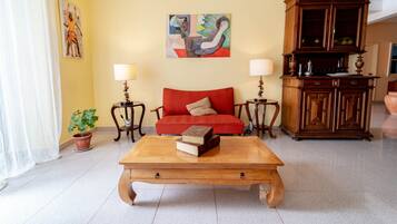 A living room with a red sofa, wooden coffee table, two side tables with lamps, a cabinet, and a painting on the wall.