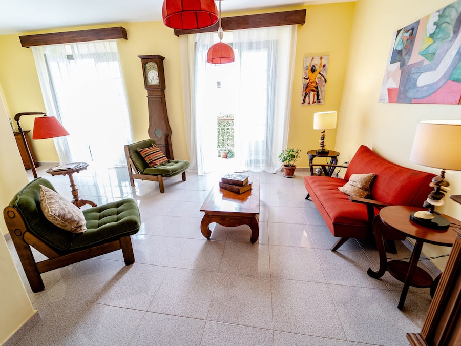 Een woonkamer met een groene fauteuil, een rode bank, een houten salontafel en een rode lamp.