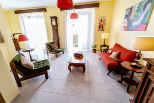 Una sala de estar con un sillón verde, un sofá rojo, una mesa de centro de madera y una lámpara roja.
