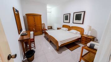 Un dormitorio con cama, muebles de madera, un escritorio, una silla, un armario y una mesita de noche con lámpara.