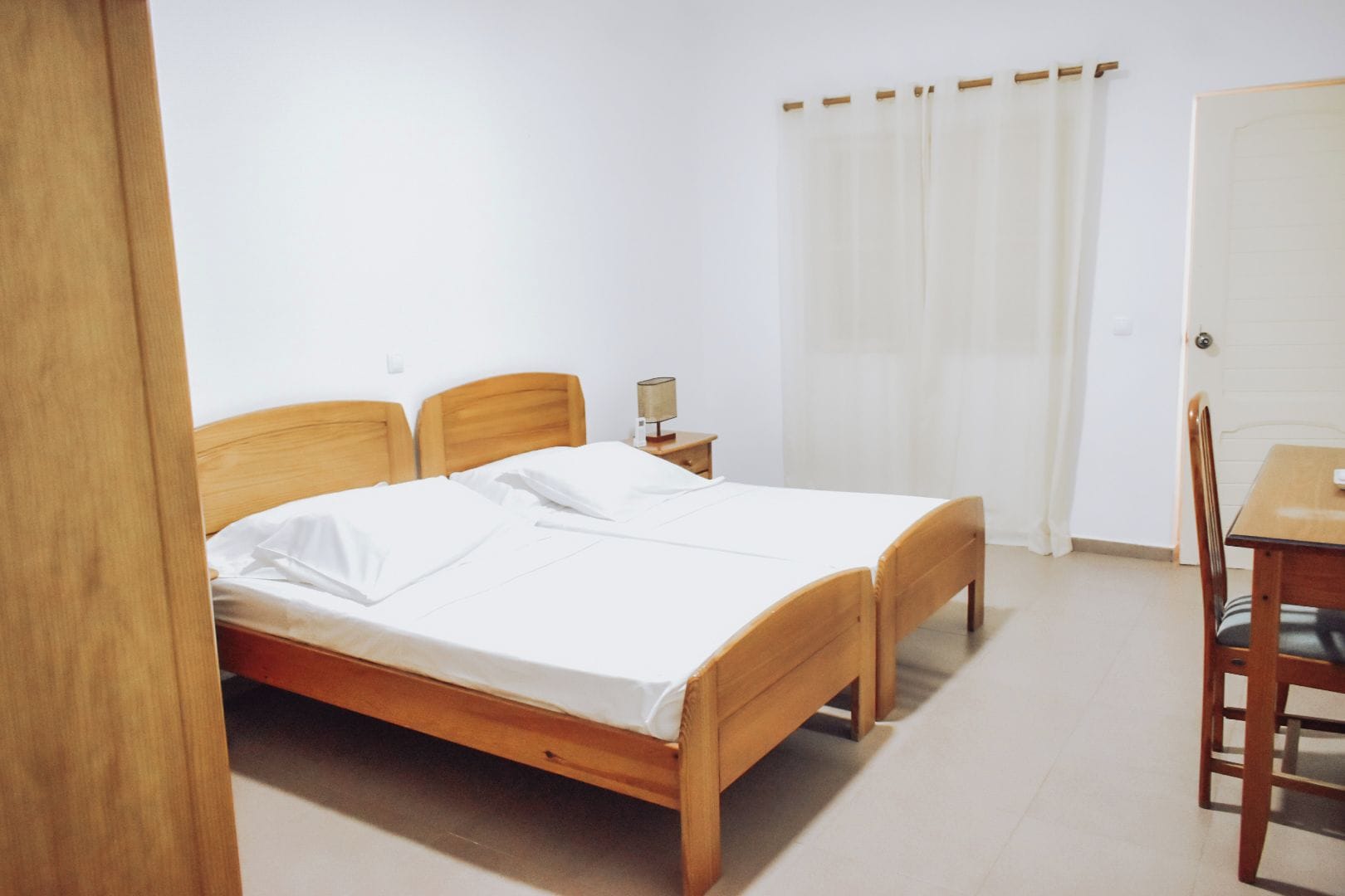 Une pièce avec un lit en bois, une table de chevet avec une lampe, une chaise et une porte.