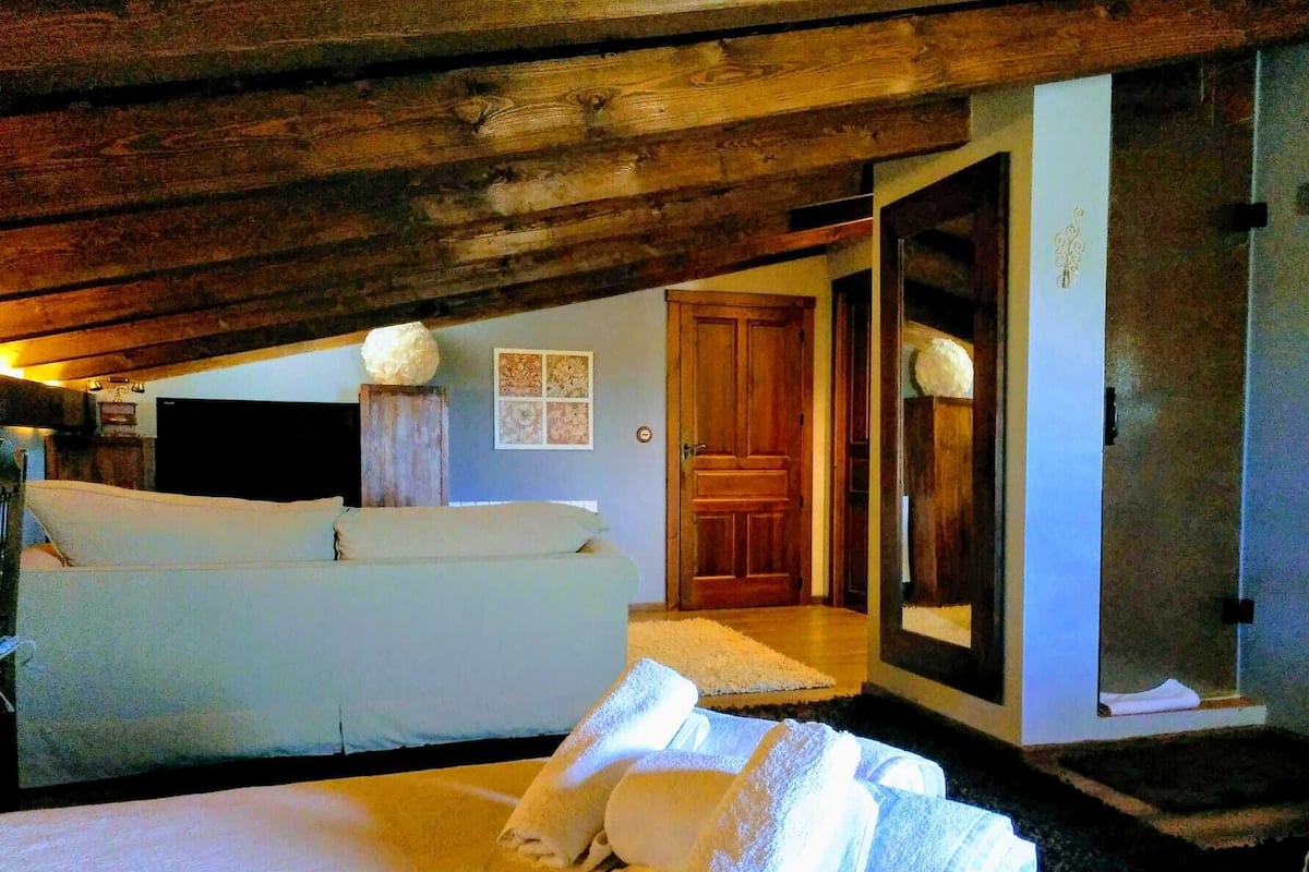 Una habitación con cama, techo de madera, una puerta y una pared con un cuadro enmarcado.