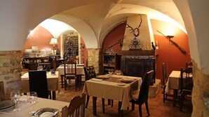 Un coin repas avec des tables préparées pour deux personnes, une cheminée et un mur en pierre.