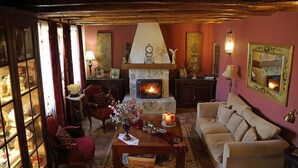 Un salon chaleureux avec une cheminée, des fauteuils rouges, un canapé et une table agrémentée d’un vase et de bougies.