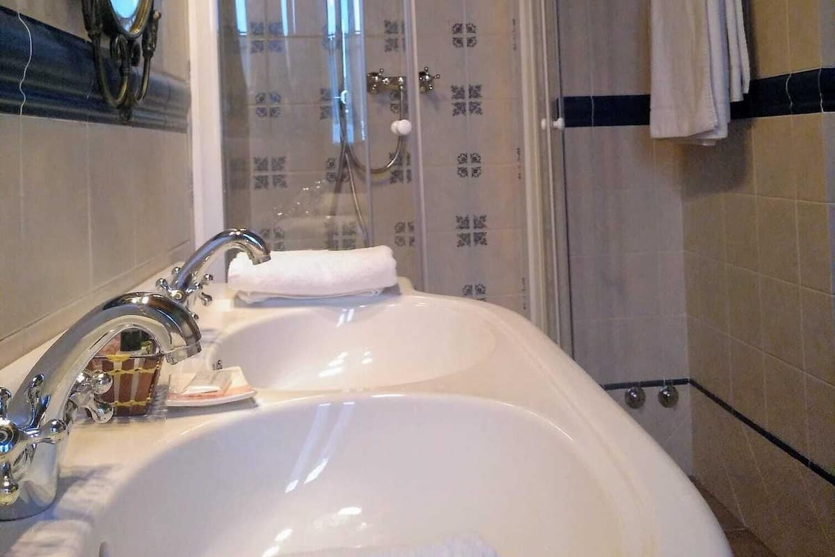 Un baño con un lavamanos blanco, una ducha con cerramiento de vidrio y un espejo con detalles ornamentales.