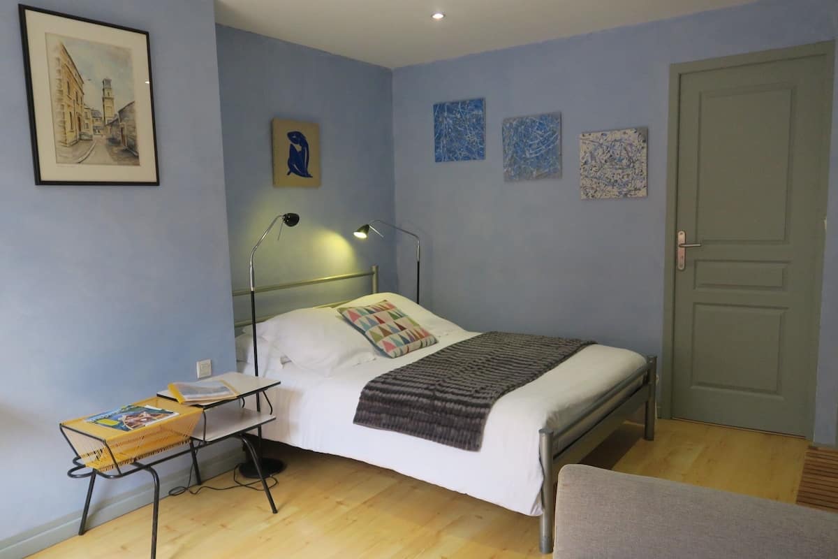 A bedroom with a bed, bedside table, lamp, and a chair.