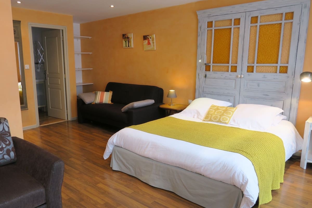 A bedroom with a large bed, a sofa, a chair, and a wardrobe.