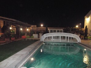 A swimming pool with a white arch bridge, surrounded by outdoor seating and potted plants.