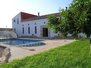 A building with a swimming pool, a red roof, and a well-maintained lawn.