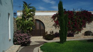 A stone building with a large arched entrance, surrounded by a well-maintained garden with various plants and a pathway leading to the entrance. - Casa Rurales Ventaseca (Mazarron)