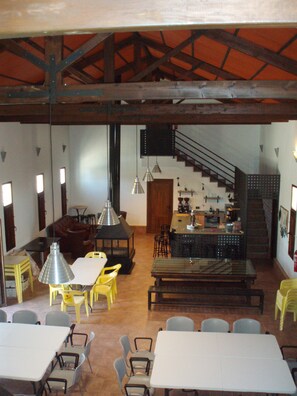 A spacious dining area with high ceilings and exposed beams, a kitchen with a bar, and a staircase leading to an upper level.