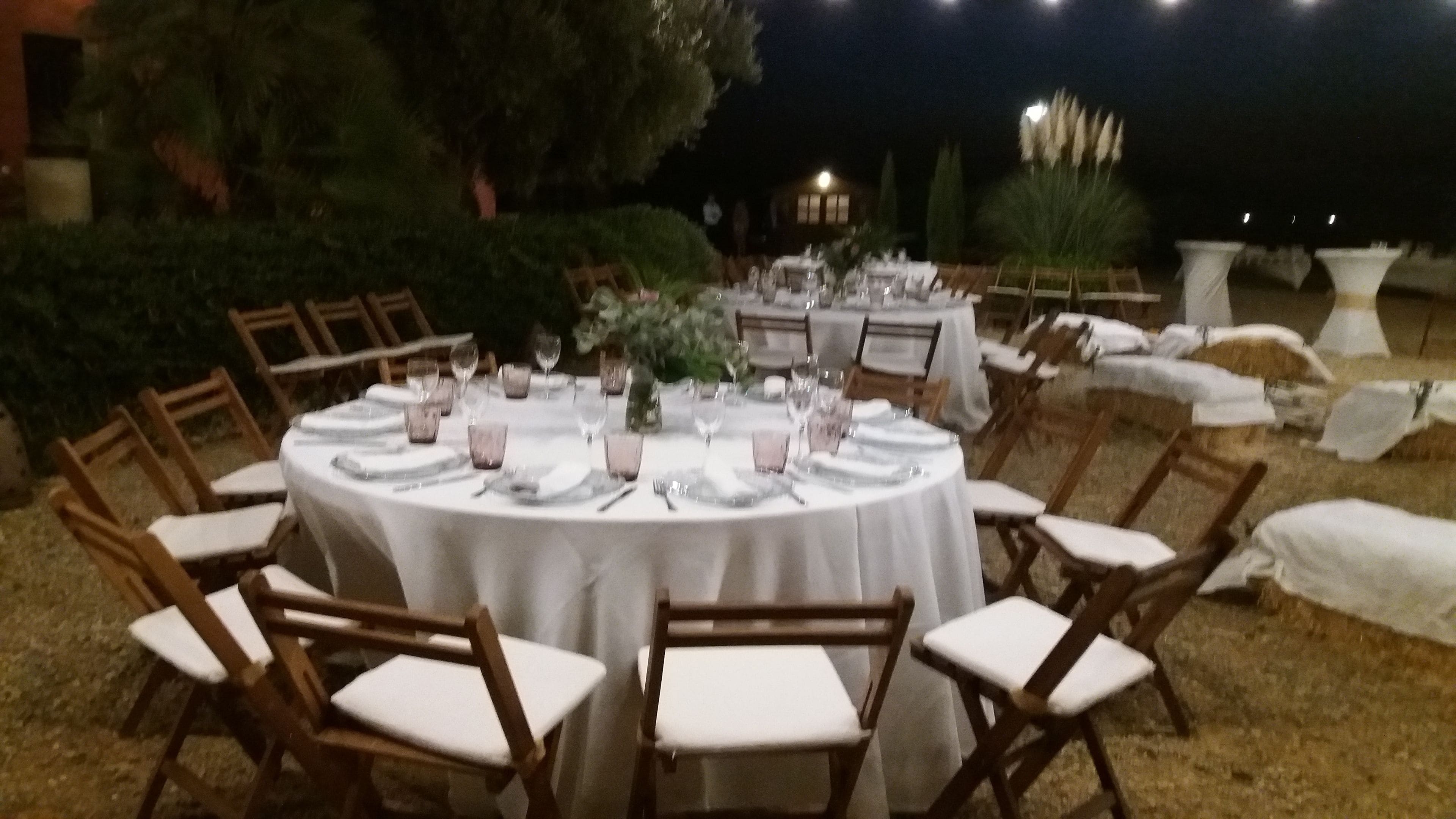Un área de comedor al aire libre con mesas redondas dispuestas para una comida, rodeada de sillas de madera.