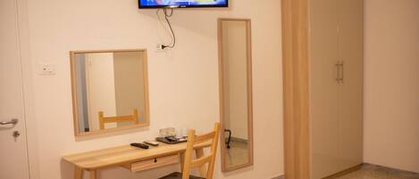 Ein Schlafzimmer mit Schreibtisch aus Holz, Stuhl und einem an der Wand befestigten Fernseher.