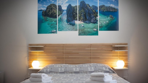 Een slaapkamer met een bed, twee bedlampen en drie ingelijste foto’s van een kustlandschap.