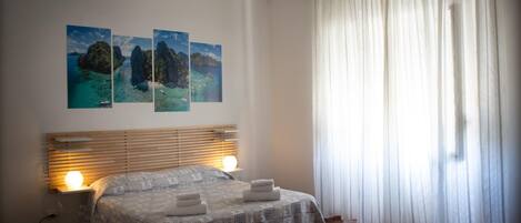 Un dormitorio con cama, mesita de noche, lámpara y tres cuadros en la pared.