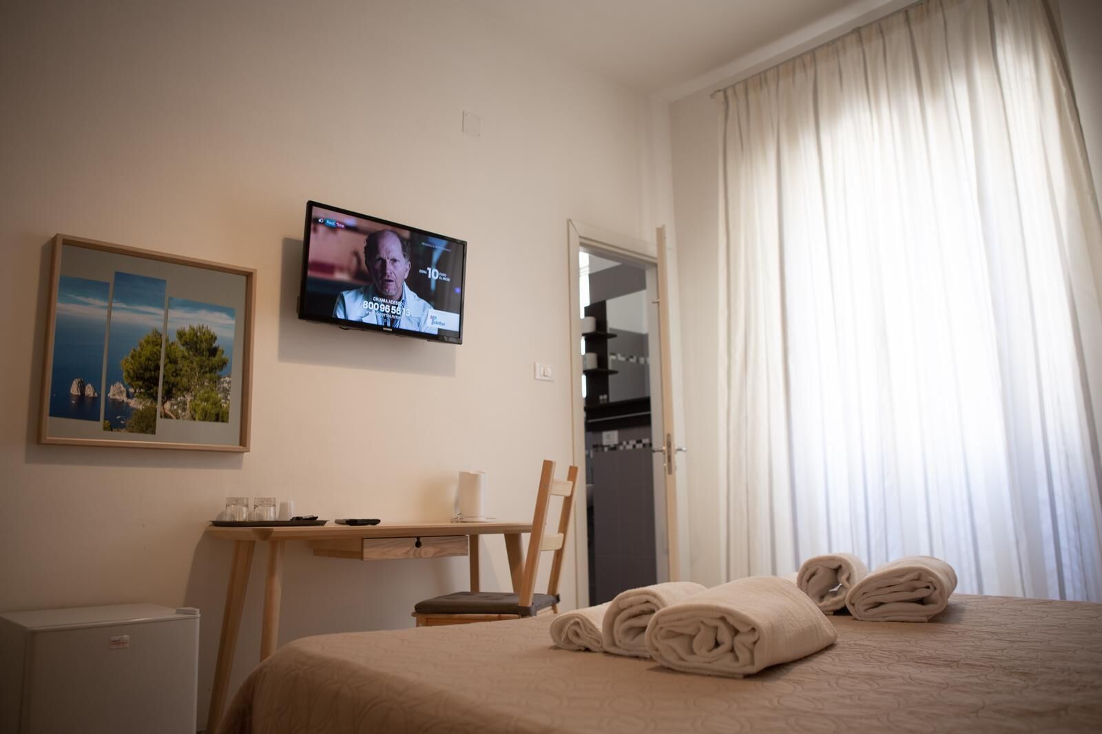 A hotel room with a bed, a desk with a chair, a television, and a window with curtains.