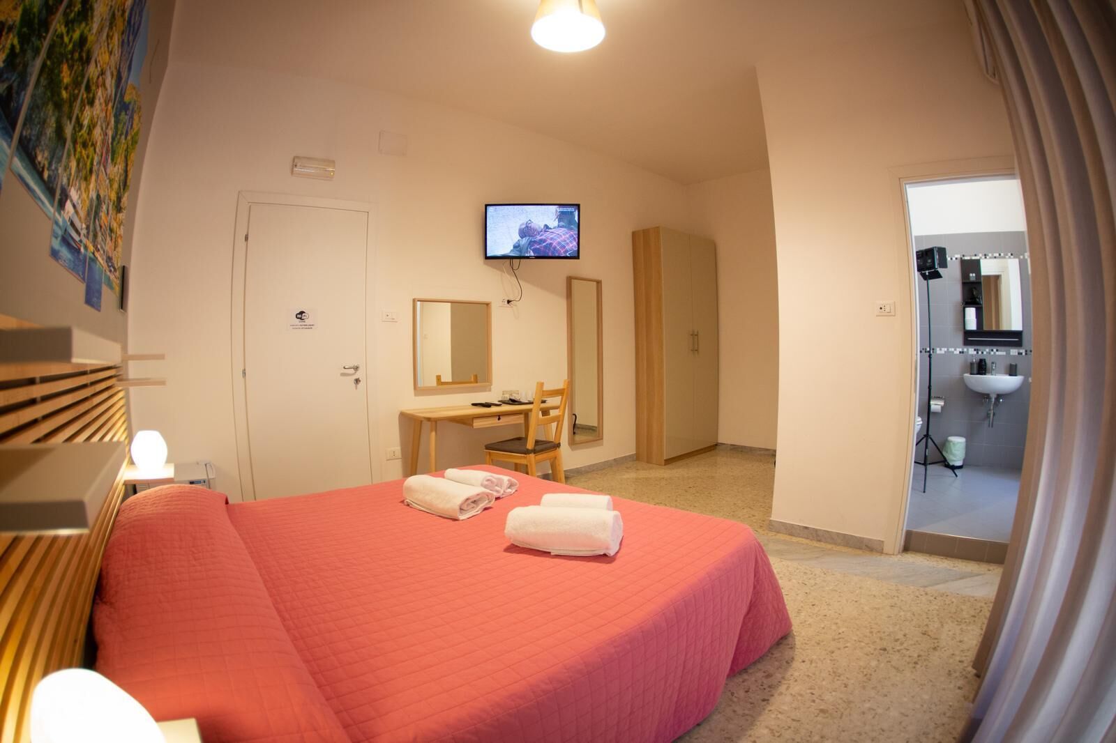 Habitación de hotel con cama, escritorio, silla, televisión y baño visible a través de una puerta abierta.