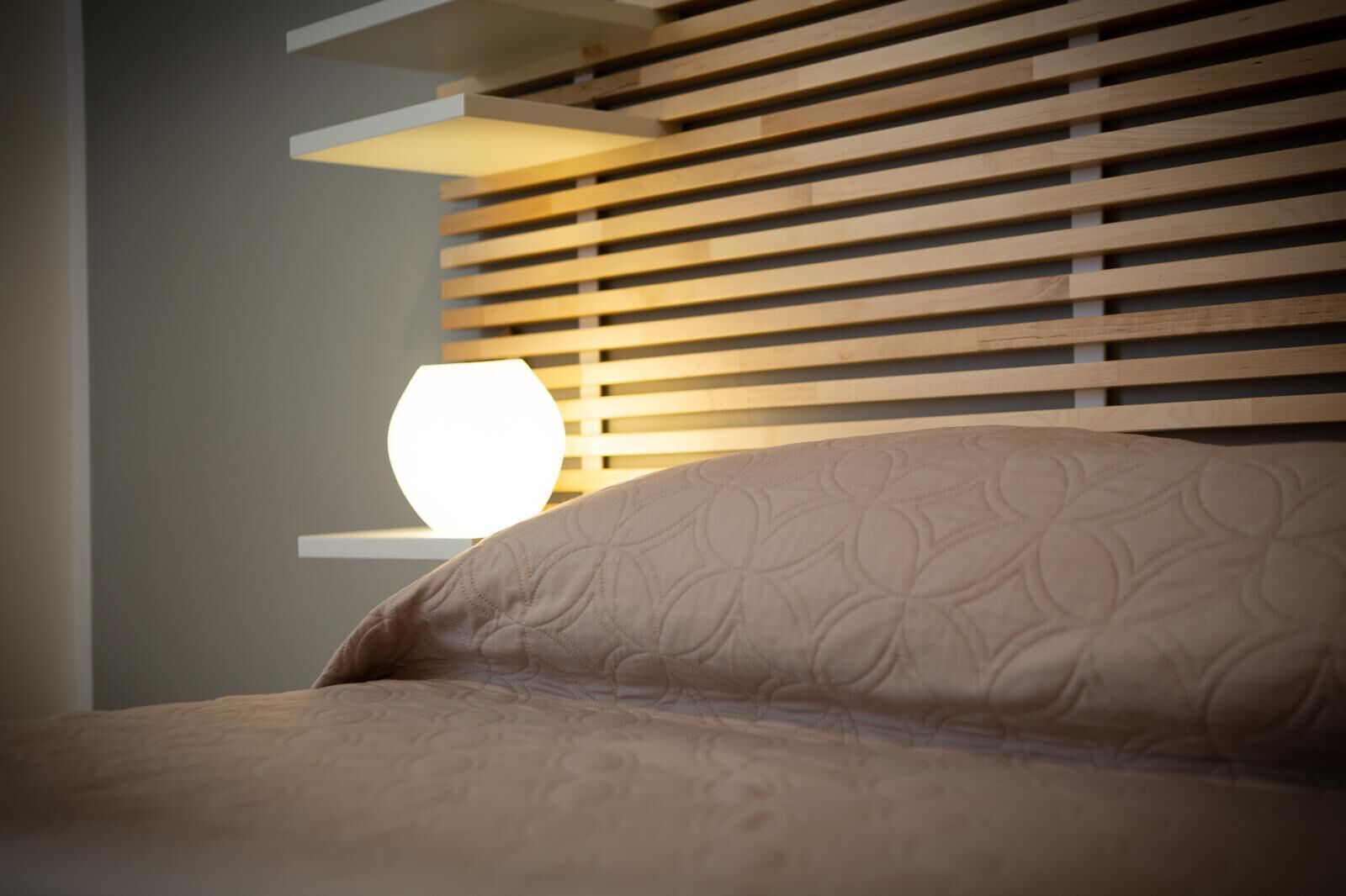A bedroom with a bed, a bedside lamp, and a wooden slat headboard.