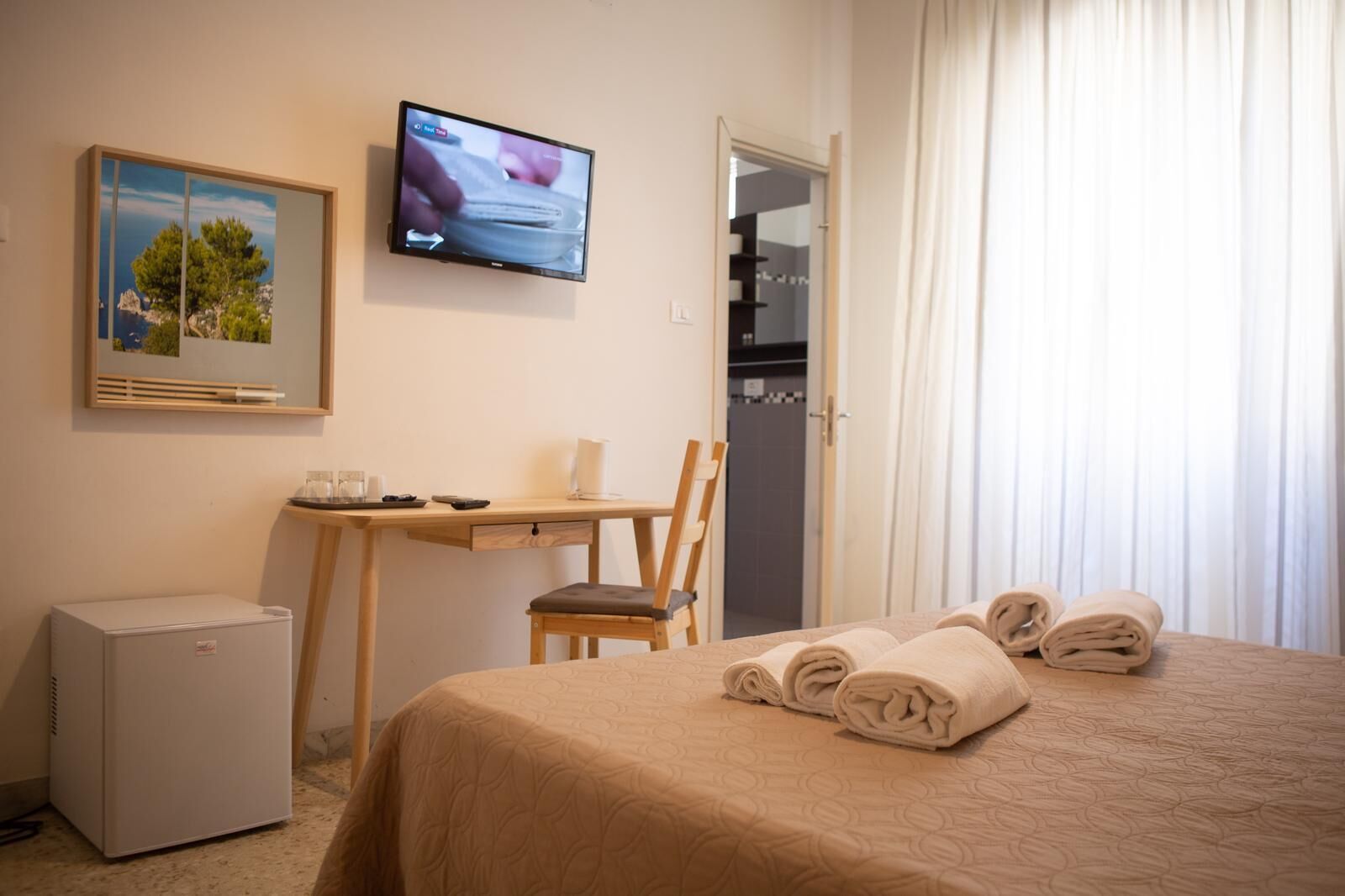 A hotel room with a bed, a desk, a chair, a television, and a small refrigerator.