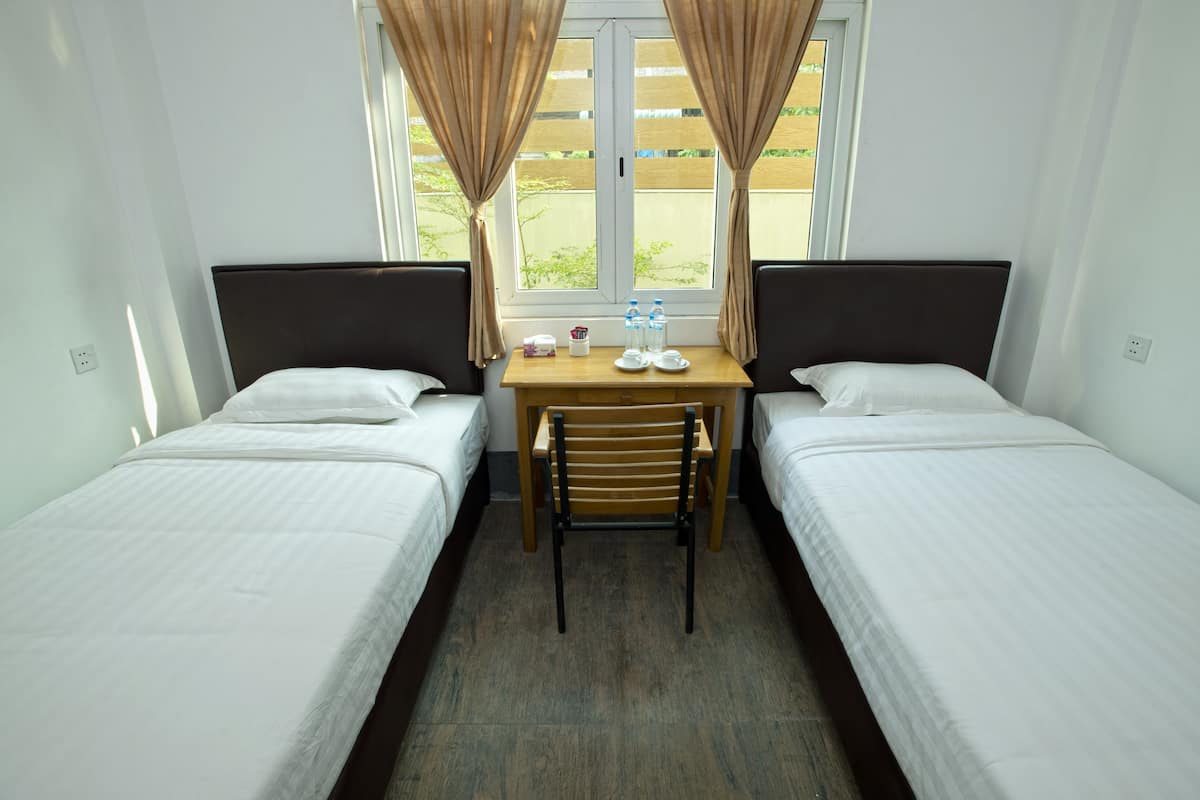 Une chambre avec deux lits simples, une table en bois avec une chaise et une fenêtre avec des rideaux.