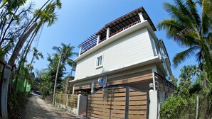 A two-story building with a balcony, a garage, and a dirt road leading to it.