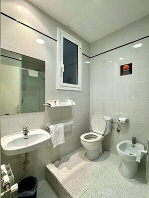 A modern bathroom with a sink, toilet, bidet, and a window above the toilet. - Pensión Peiró (Barcelona)