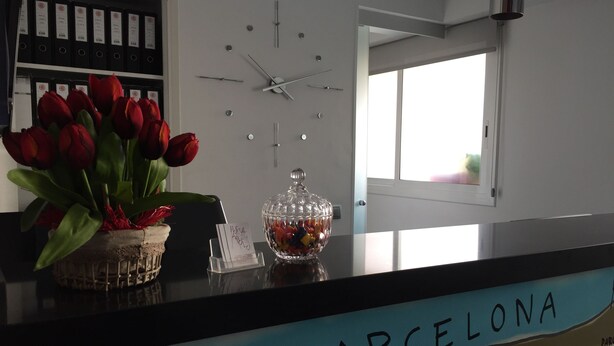 En reception med et ur, en vase med røde tulipaner, en glas skål med slik, og et skilt med teksten "BARCELONA".