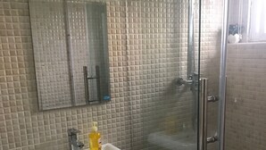 A bathroom with a glass-enclosed shower, a white sink, and a mirror above the sink. - Grand Condo (Lekki)