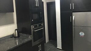 A kitchen with black cabinets, a stainless steel refrigerator, and a microwave. - Grand Condo (Lekki)