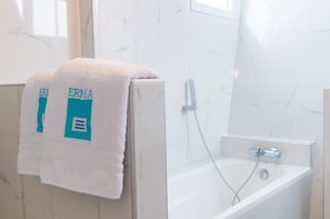 A bathroom with a white bathtub, a towel with "ERMA" on it, and a marble wall.
