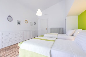 A modern hotel room with two beds, a white dresser, a radiator, and a green accent wall.