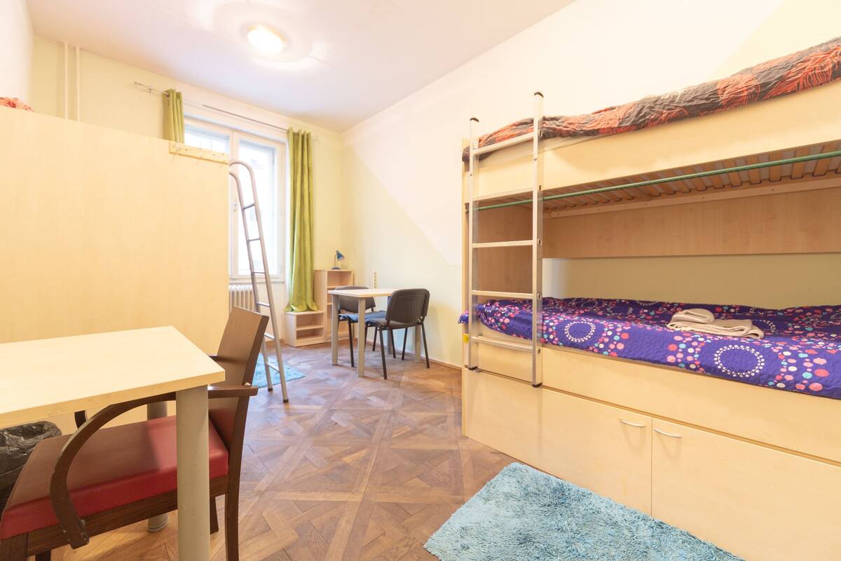 A dormitory room with bunk beds, a desk, and a chair.