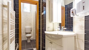 A bathroom with a white sink, mirror, and toilet. There is a window above the toilet and a radiator on the left. - Ana Hostel (Ljubljana)