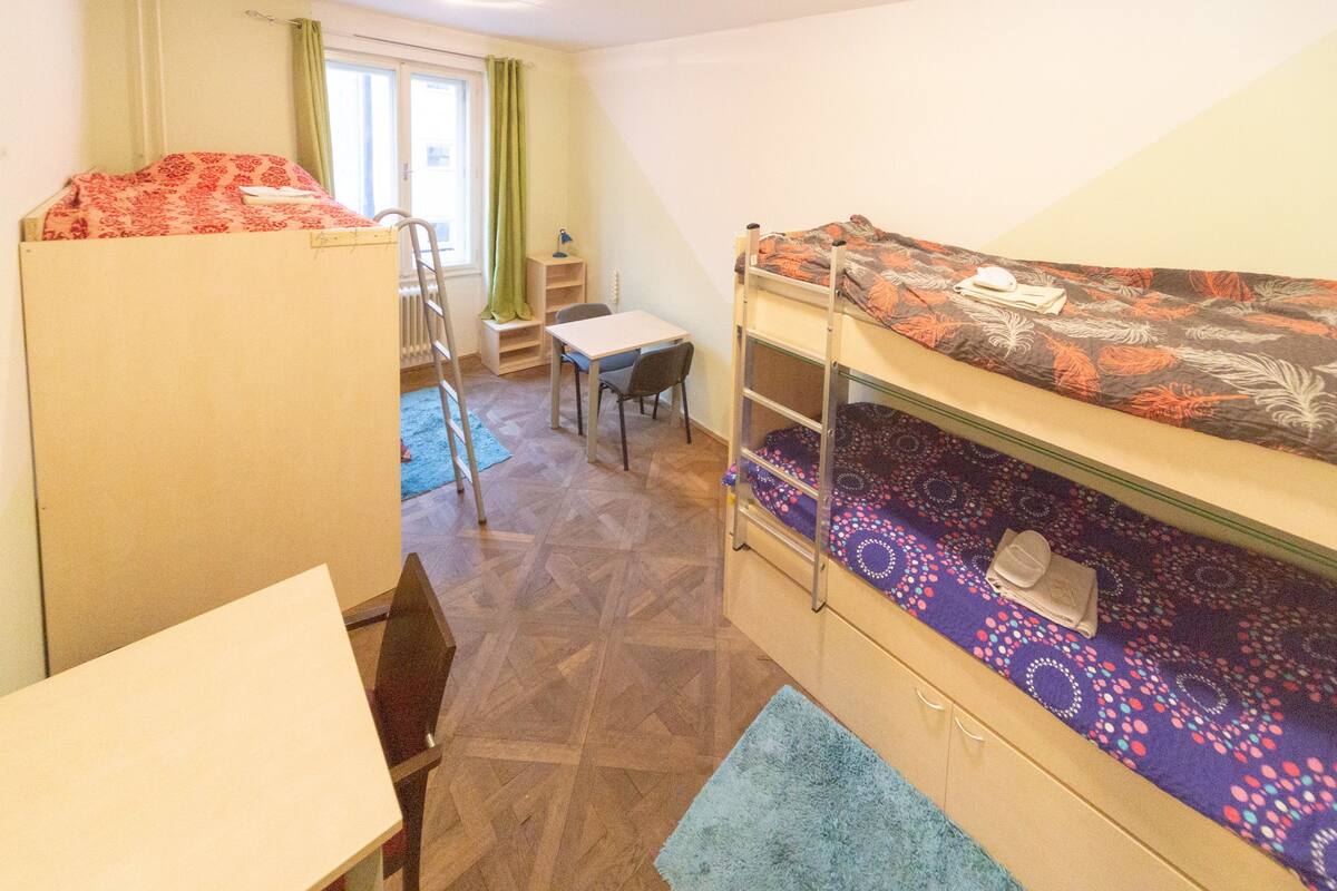 A dormitory room with bunk beds, a desk, a chair, and a radiator.
